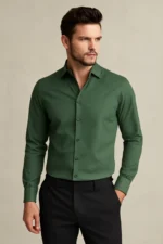 Man wearing a solid bottle green slim fit full-sleeve shirt with black formal trousers against a neutral background.