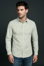 Man wearing a slim fit, full-sleeve shirt in a light sage green with a subtle micro print, paired with blue jeans against a dark background.