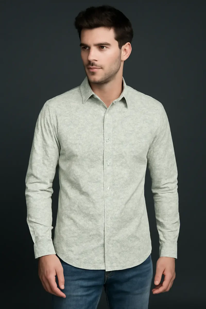 Man wearing a slim fit, full-sleeve shirt in a light sage green with a subtle micro print, paired with blue jeans against a dark background.