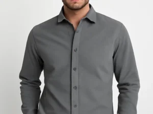 Man wearing a solid charcoal grey slim fit full-sleeve shirt with black trousers, standing with one hand in his pocket against a white background.