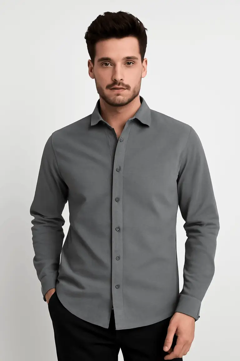 Man wearing a solid charcoal grey slim fit full-sleeve shirt with black trousers, standing with one hand in his pocket against a white background.