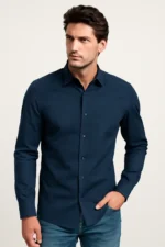Man looking to the side, wearing a slim fit navy blue full-sleeve shirt with a subtle geometric dobby pattern, paired with blue jeans.